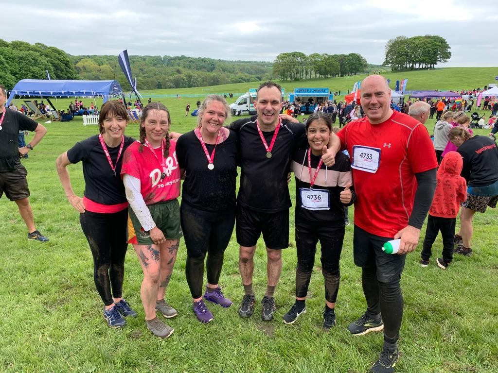 5 members of Team Bailoran after a muddy race, with Ellie Brown from Leeds Baby Bank, all wearing medals on pink ribbon.